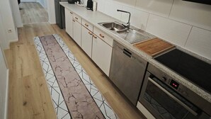 A modern kitchen with white cabinets, a stainless steel sink, a built-in oven, and a wooden countertop. - Charming Family Apartment in Wutöschingen With Garden View (Wutoeschingen)
