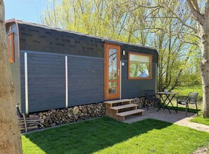 A small, single-story building with a dark exterior, a wooden door, and a window. - Tiny House Säbelschnäbler Gut Osterhausen Butjadingen - Glamping and nature (Butjadingen)