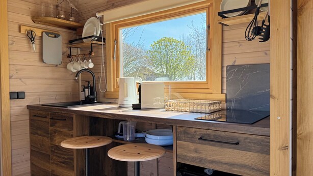 Una cocina compacta con ventana, armarios de madera, un lavamanos, taburetes y lavavajillas.