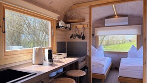 Un interior compacto de madera con kitchenette, dos camas y ventanas amplias que dan a vistas del exterior.