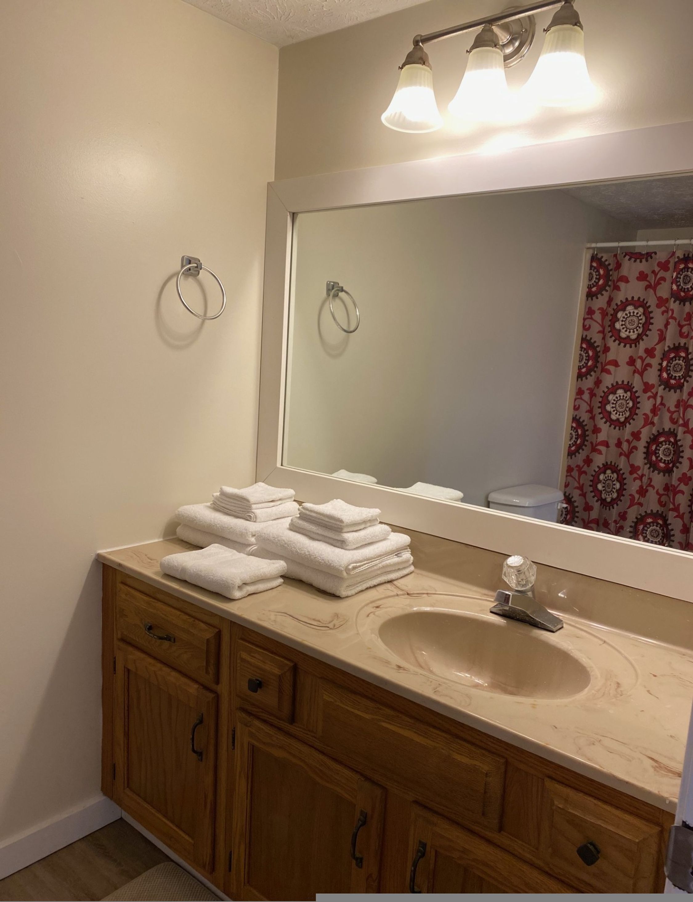 Une salle de bain avec un lavabo beige, un meuble-lavabo en bois, deux porte-serviettes et un miroir au-dessus du lavabo.