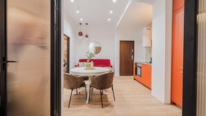 Eine moderne Küche mit orangefarbenen Schränken, ein weißer Essbereich mit einem runden Tisch und zwei Stühlen sowie ein rotes Sofa.
