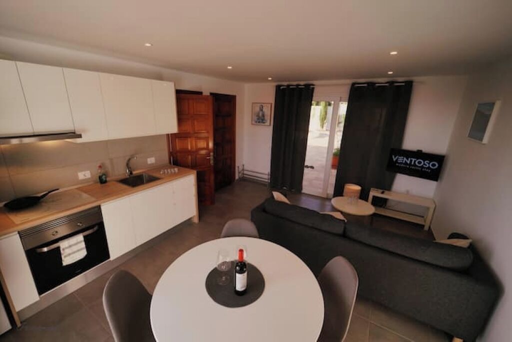 Una cocina moderna con armarios blancos, una mesa de comedor con dos sillas y un sofá en la sala de estar.