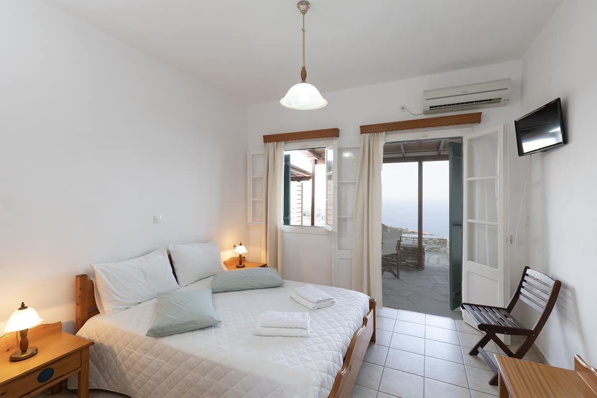 A bedroom with a bed, bedside table, lamp, and a TV on the wall.