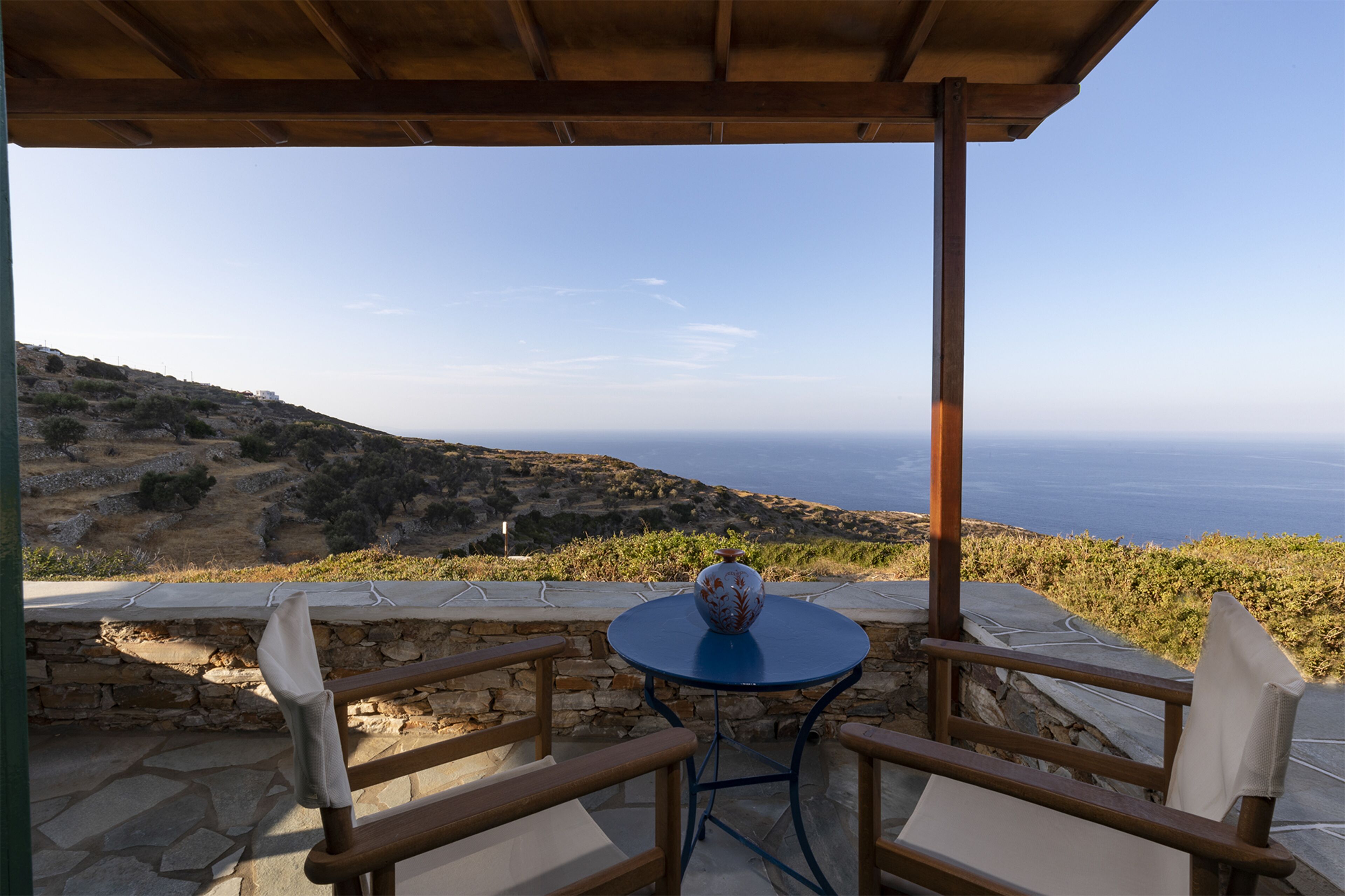 A patio with a table and chairs overlooking a scenic view of the sea and hills.