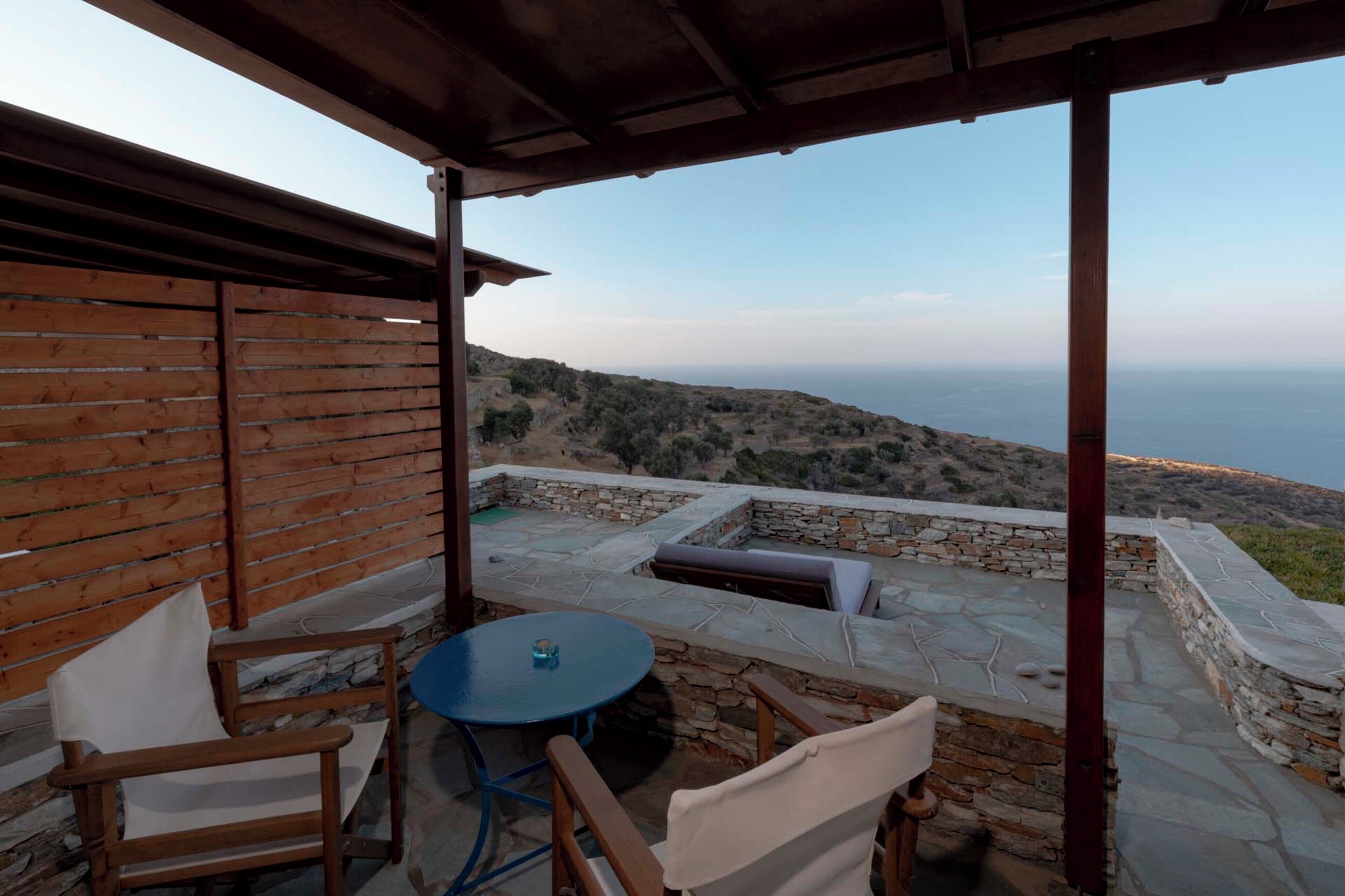 Un espacio al aire libre techado con paredes de piedra, una mesa redonda y sillas de madera.