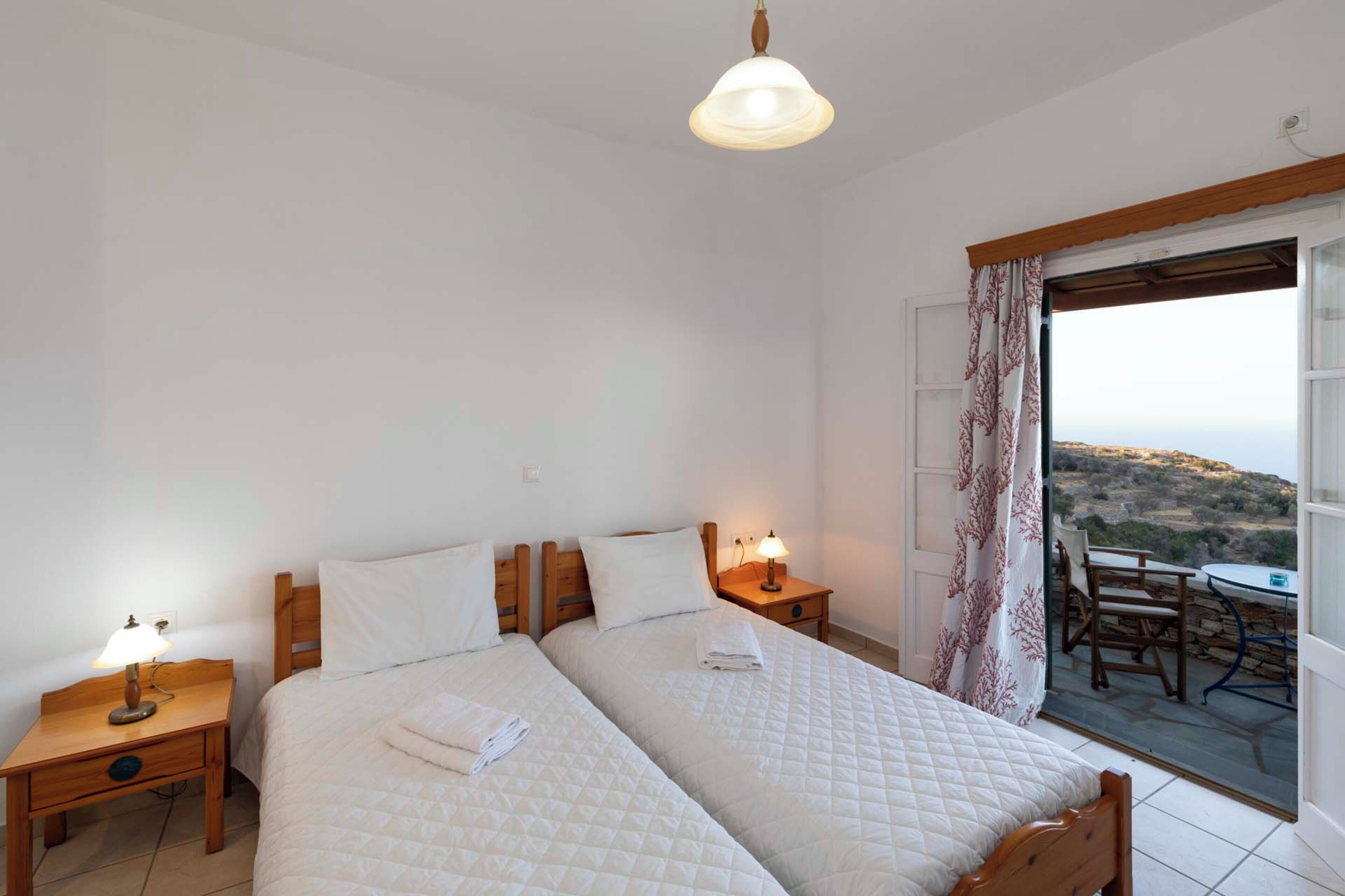 Een slaapkamer met twee bedden, een balkon met een tafel en stoelen, en uitzicht op het landschap.