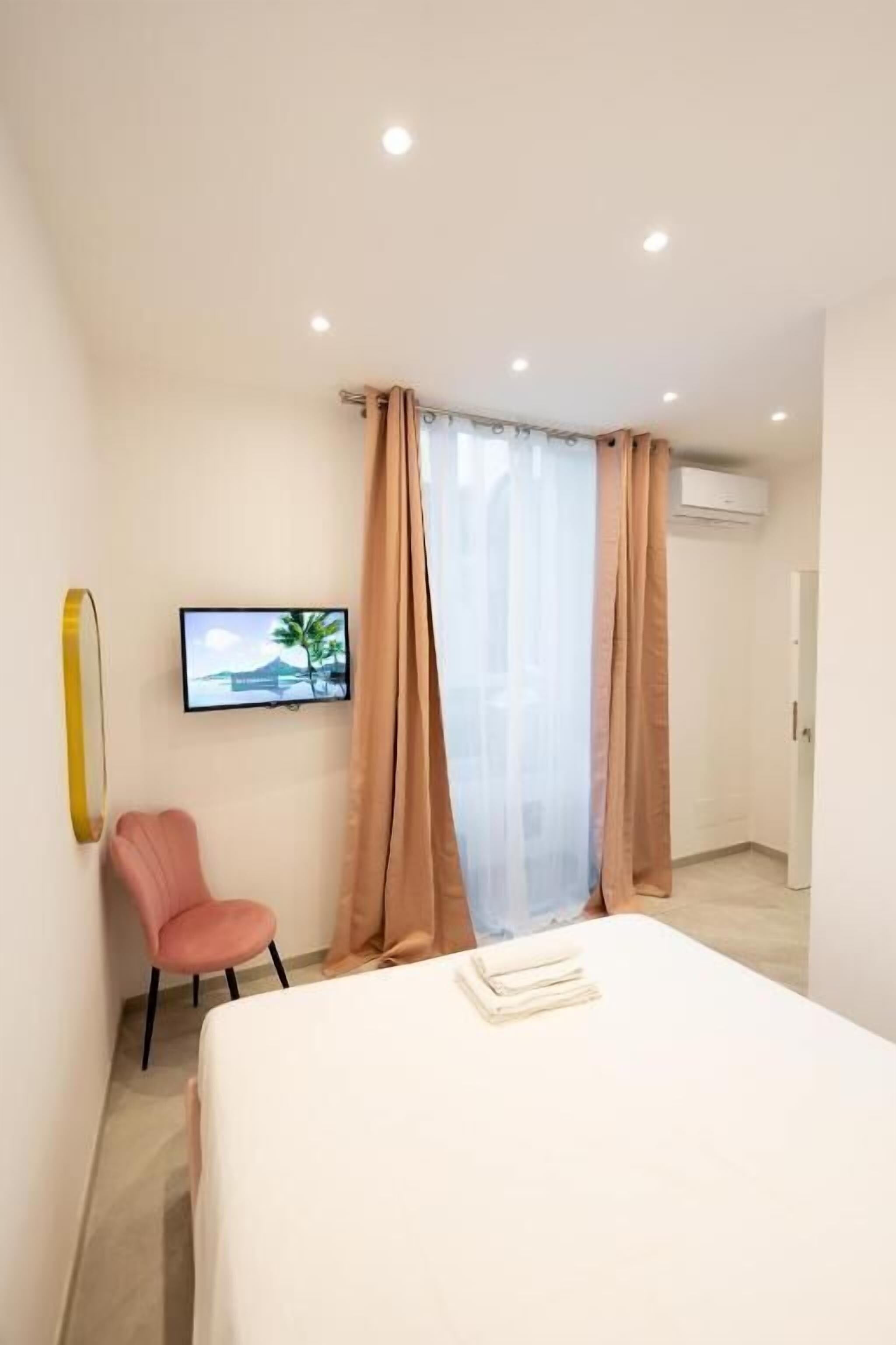 A modern hotel room with a bed, a television mounted on the wall, a chair, and a window with curtains.