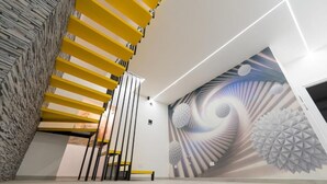 A modern interior with a spiral staircase, a mural with geometric patterns, and a bench. - Suites Gaudioso Napoli Center (Naples)