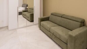 A modern room with a green sofa, a large mirror, and a bed in the background. - Suites Gaudioso Napoli Center (Naples)