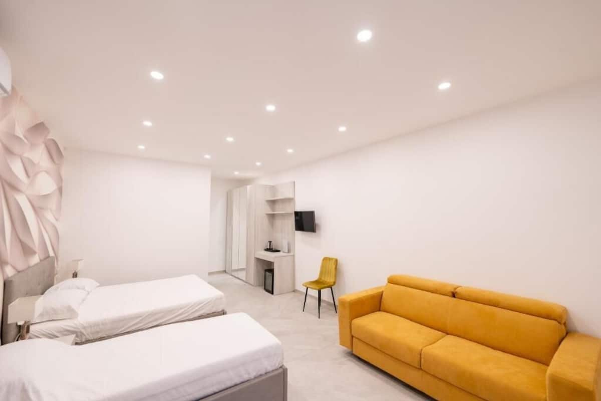 A modern bedroom with two beds, a yellow sofa, a desk, and a TV.