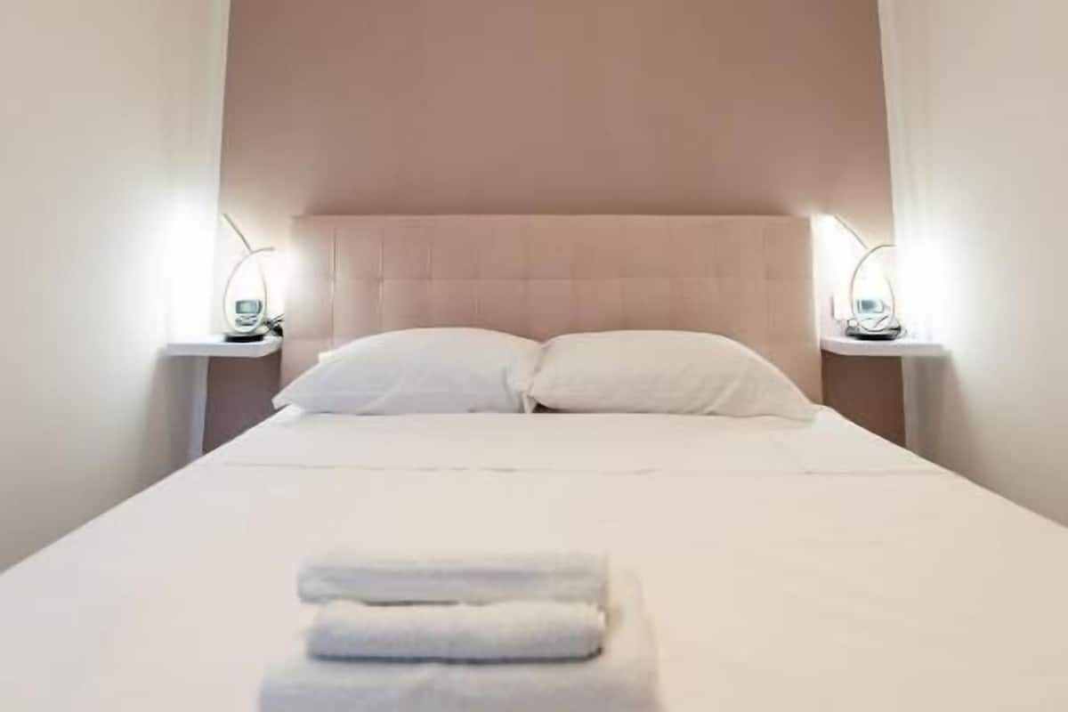 A neatly made bed with pillows and folded towels, two bedside lamps, and a headboard.