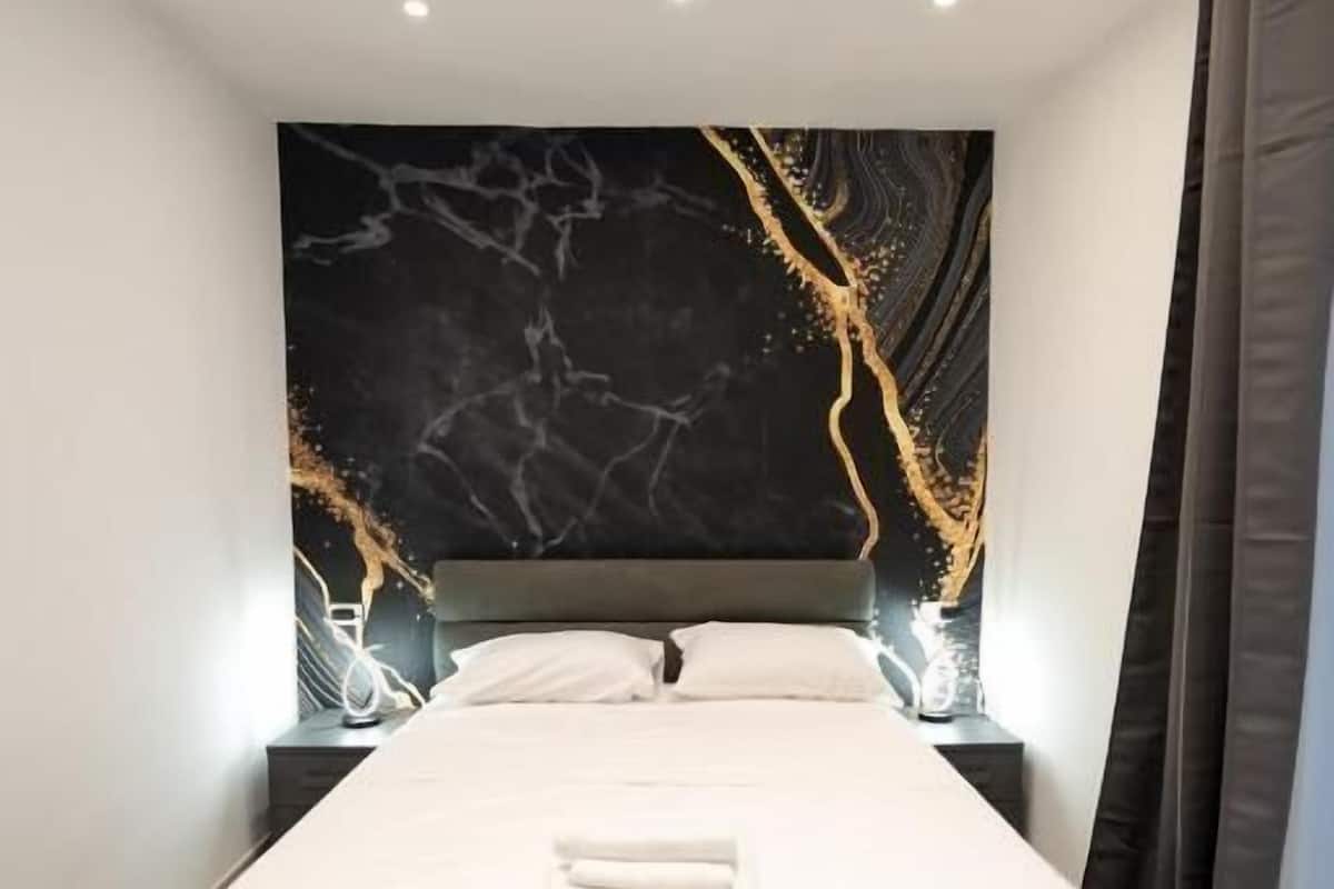 A modern bedroom with a large bed, a marble-patterned wall, and recessed ceiling lights.