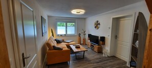 Un salon avec un canapé, une table basse, un téléviseur et une fenêtre équipée de stores.