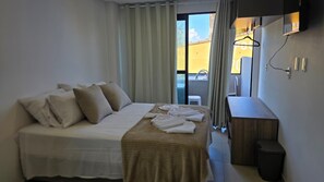 Een hotelkamer met een bed, een klein bureau, een prullenbak en uitzicht op buiten.