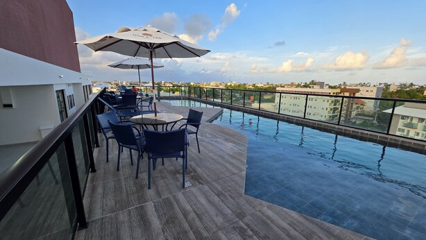 A rooftop pool area with lounge chairs and umbrellas, offering a view of the cityscape. - Studio piscina privativa 10 by La Playa (Ipojuca)