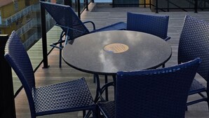 A rooftop terrace with round tables and blue chairs, overlooking a cityscape during sunset. - Studio piscina privativa 10 by La Playa (Ipojuca)