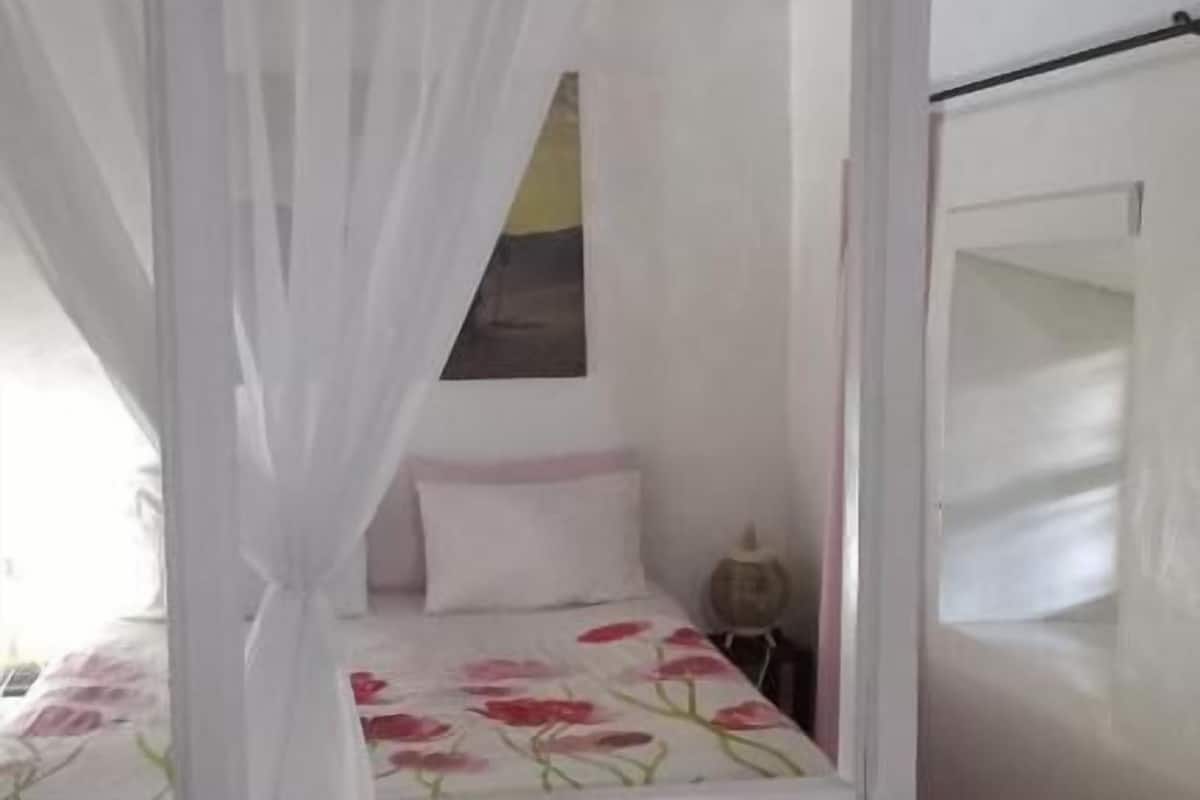 Un dormitorio con cama con dosel, una mesita de noche pequeña y una ventana con un cuadro.