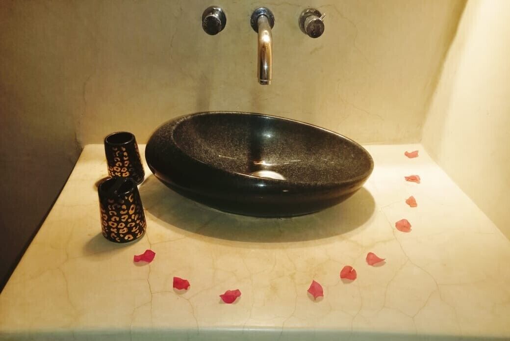A bathroom sink with a black basin and two decorative cups.