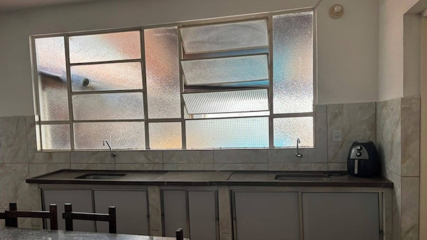 A kitchen with a large window, a sink, cabinets, and a dining table. - Pousada Recanto Alto Da Boa Vista (Cachoeira Paulista)