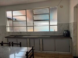 Una cocina con un ventanal grande, un lavamanos, armarios y una mesa de comedor.