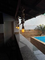 Zona de bar con mostrador y sillas, piscina con azulejos azules y techo decorado con cuerdas.