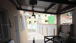 An outdoor patio with a black leather sofa, a wooden table, and a bench. - Pousada Recanto Alto Da Boa Vista (Cachoeira Paulista)
