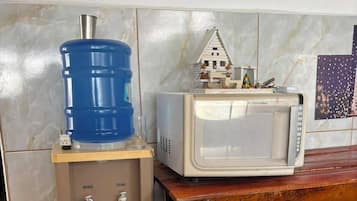 Uma kitchenette compacta com um dispensador de água, um micro-ondas e um pequeno modelo de casa sobre uma mesa de madeira.