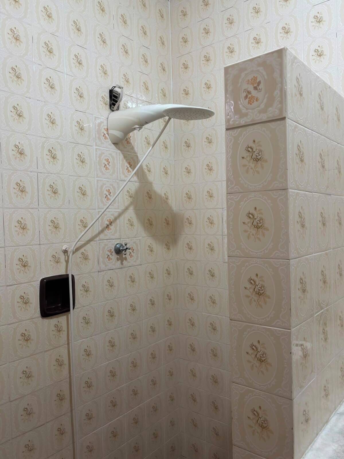 A shower with a handheld showerhead mounted on the wall, a control panel, and a small black object attached to the wall.