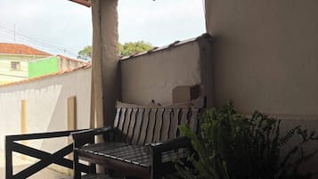 Un banco de madera bajo un porche cubierto con una planta en maceta a un lado.