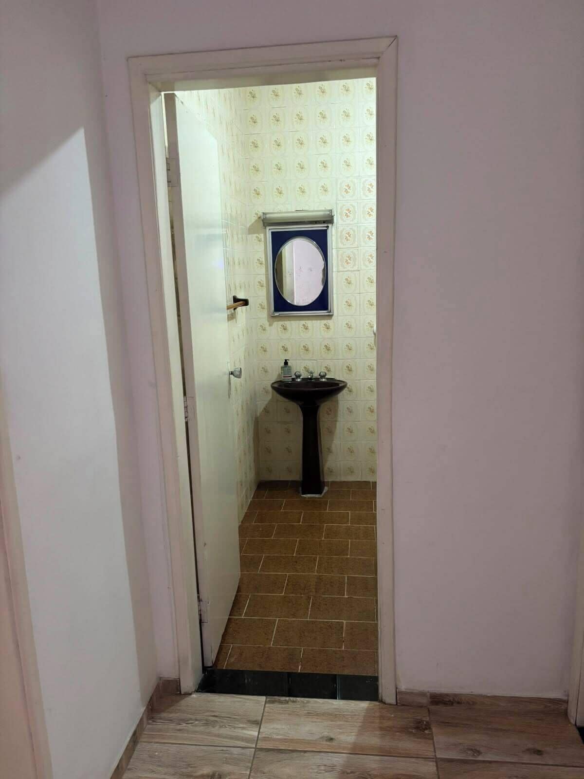 Un couloir étroit mène à une salle de bain équipée d’un lavabo et d’un miroir.