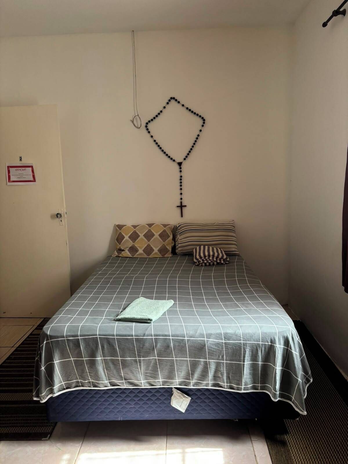 A single bed with a checkered bedspread, a pillow, and a blanket on the floor.