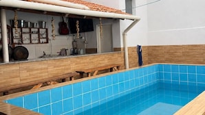 A swimming pool with a tiled deck, a covered area with kitchenware, and a wooden bench. - Pousada Recanto Alto Da Boa Vista (Cachoeira Paulista)