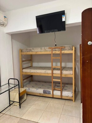 Un lit superposé avec un téléviseur fixé au-dessus, une petite table et une porte.