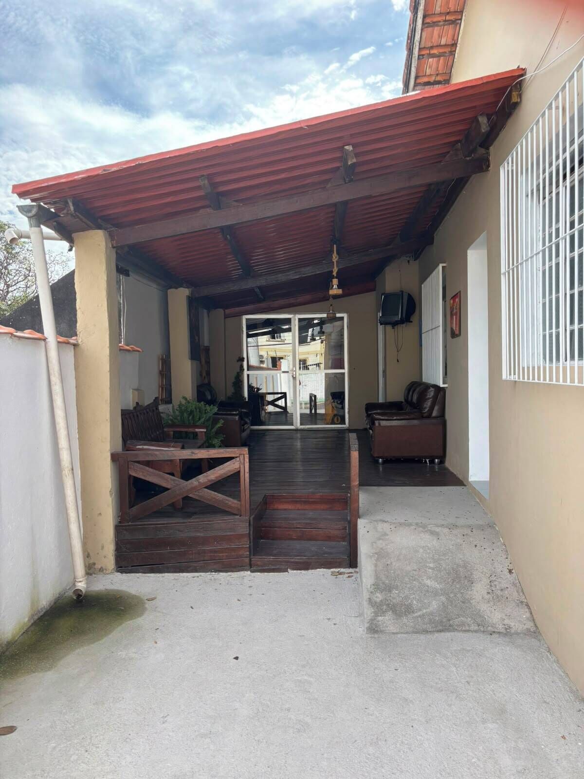 A covered outdoor area with a patio, a wooden bench, a sofa, and a television mounted on the wall.