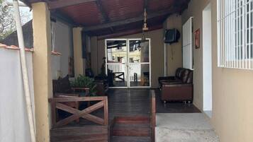 A covered outdoor area with a patio, a wooden bench, a sofa, and a television mounted on the wall.