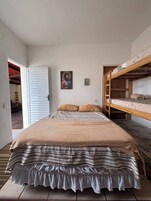 Un dormitorio con una cama litera, una cama individual con edredón a rayas, una puerta que da a otra habitación y un cuadro en la pared.