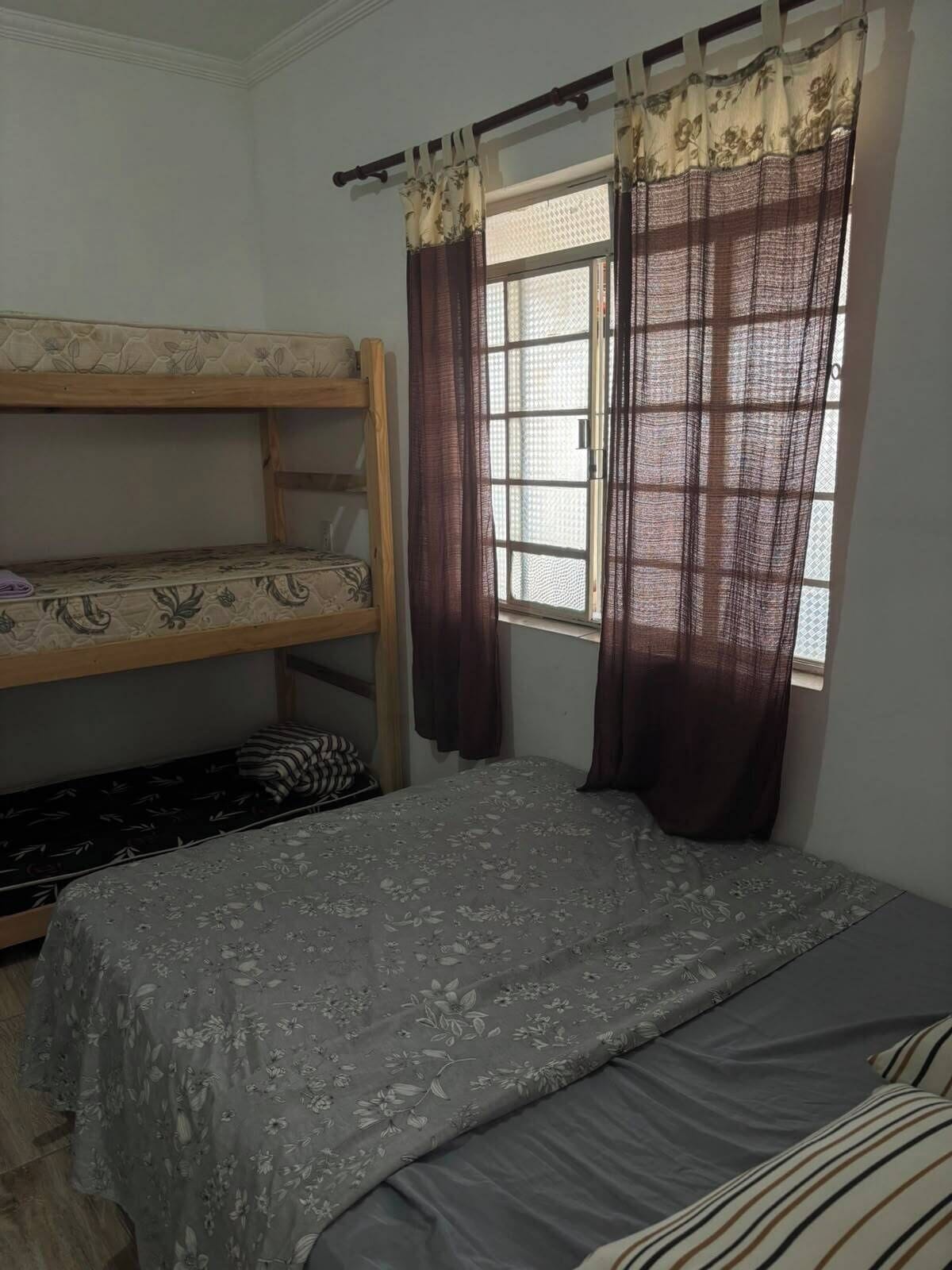 A room with a bunk bed, a window with curtains, and a bed with a floral bedspread.