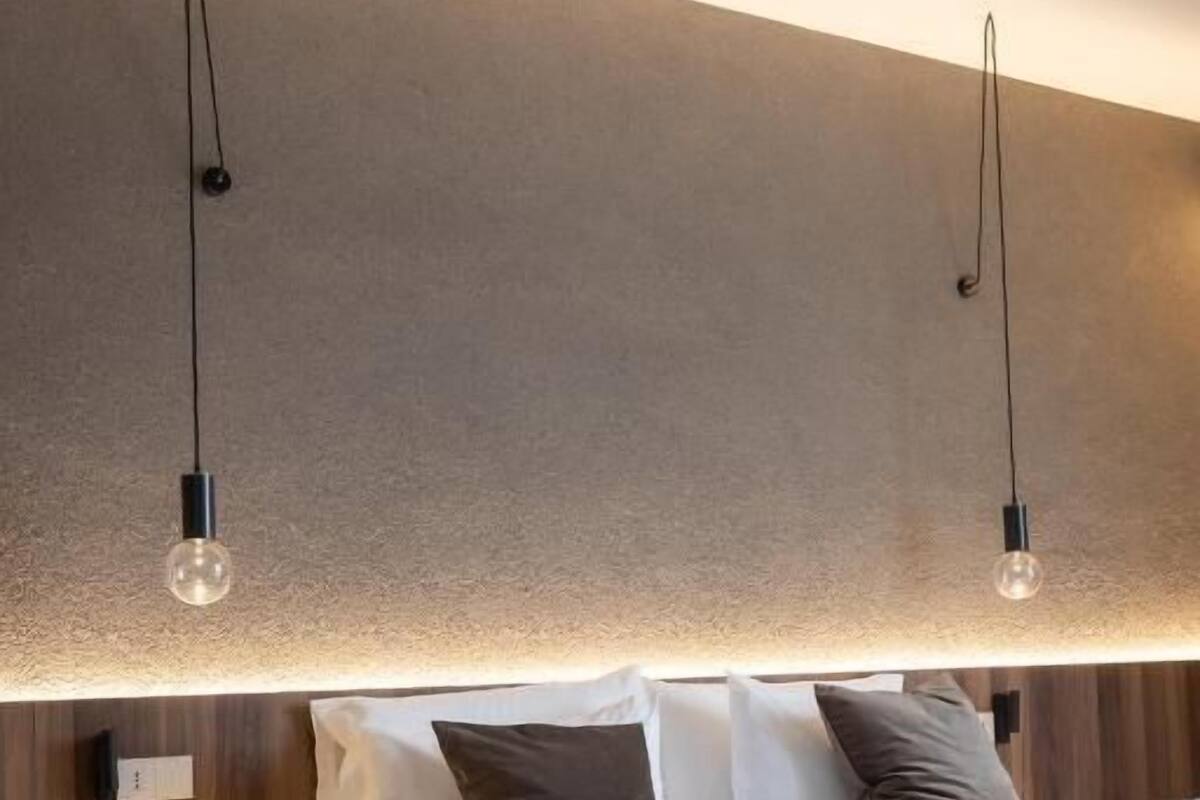 A modern bedroom with a wooden headboard, a round bedside table, and two pendant lights.