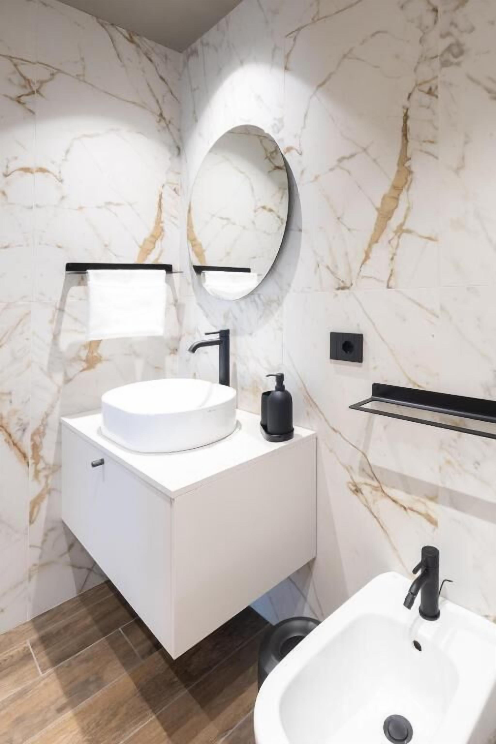 Uma casa de banho moderna com toucador branco, espelho redondo, lavatório branco e torneira preta.