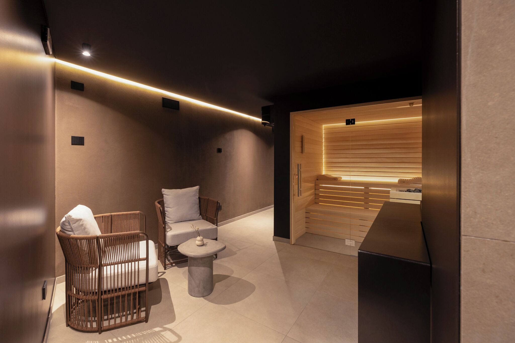 A modern bathroom with a wooden vanity, a wicker chair, a small round table, and a white sofa.