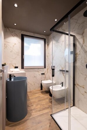 A modern bathroom with a marble wall, a large sink, a bidet, and a glass shower enclosure. - Stemor srl (Desenzano del Garda)