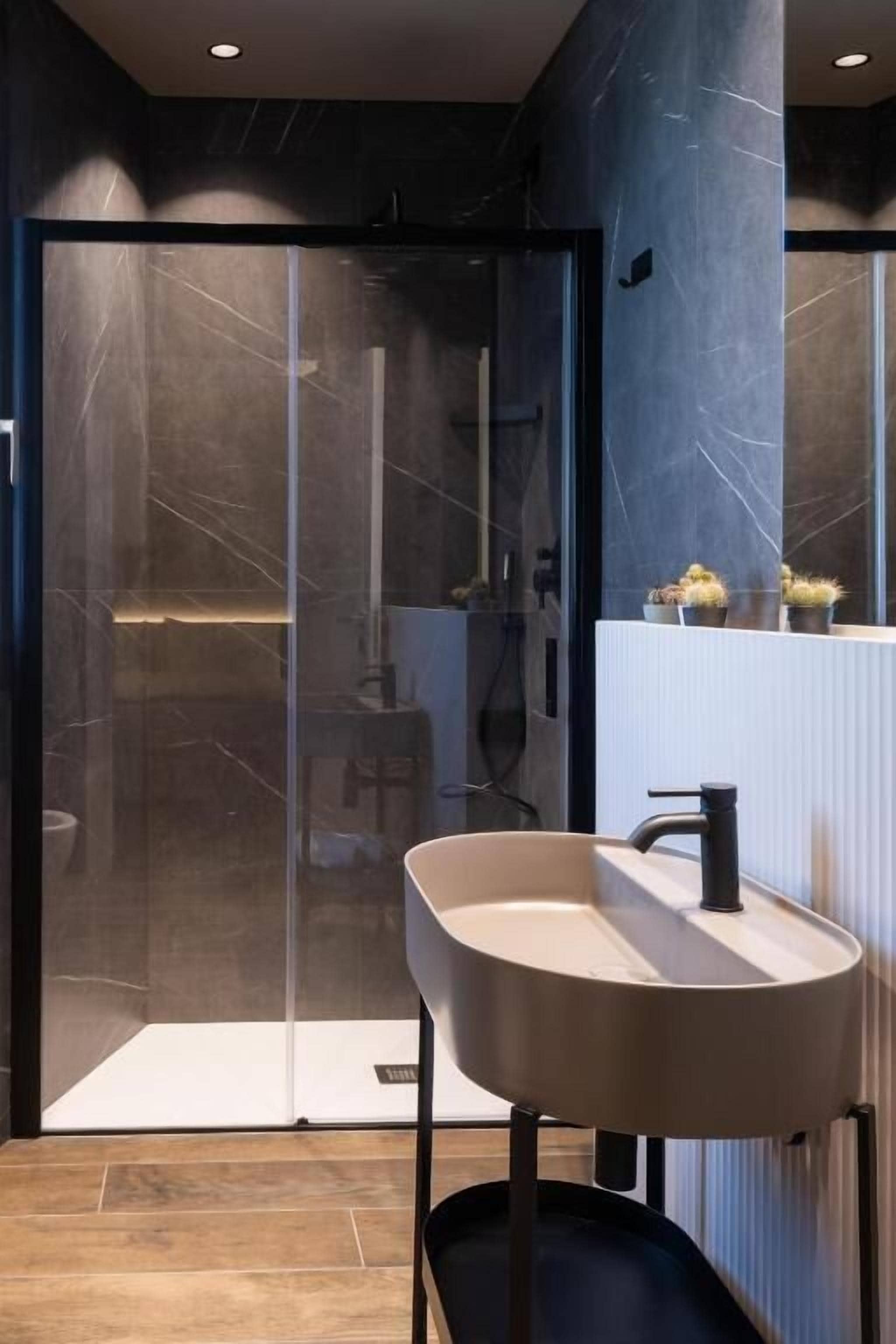 A modern bathroom with a glass shower enclosure, a minimalist sink, and a marble wall.