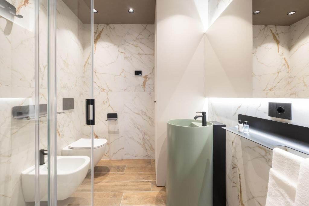 A modern bathroom with a glass shower enclosure, a white toilet, a bidet, and a green sink.