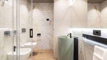 A modern bathroom with a glass shower enclosure, a white toilet, a bidet, and a green sink.