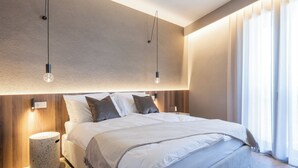 A modern bedroom with a large bed, two wall-mounted lights, a bedside table, and a window with curtains. - Stemor srl (Desenzano del Garda)