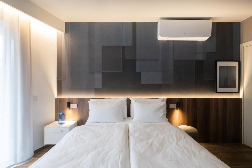 A modern hotel room with a large bed, bedside tables, a wall-mounted air conditioner, and a framed picture.