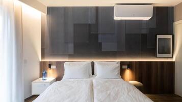 A modern hotel room with a large bed, bedside tables, a wall-mounted air conditioner, and a framed picture.