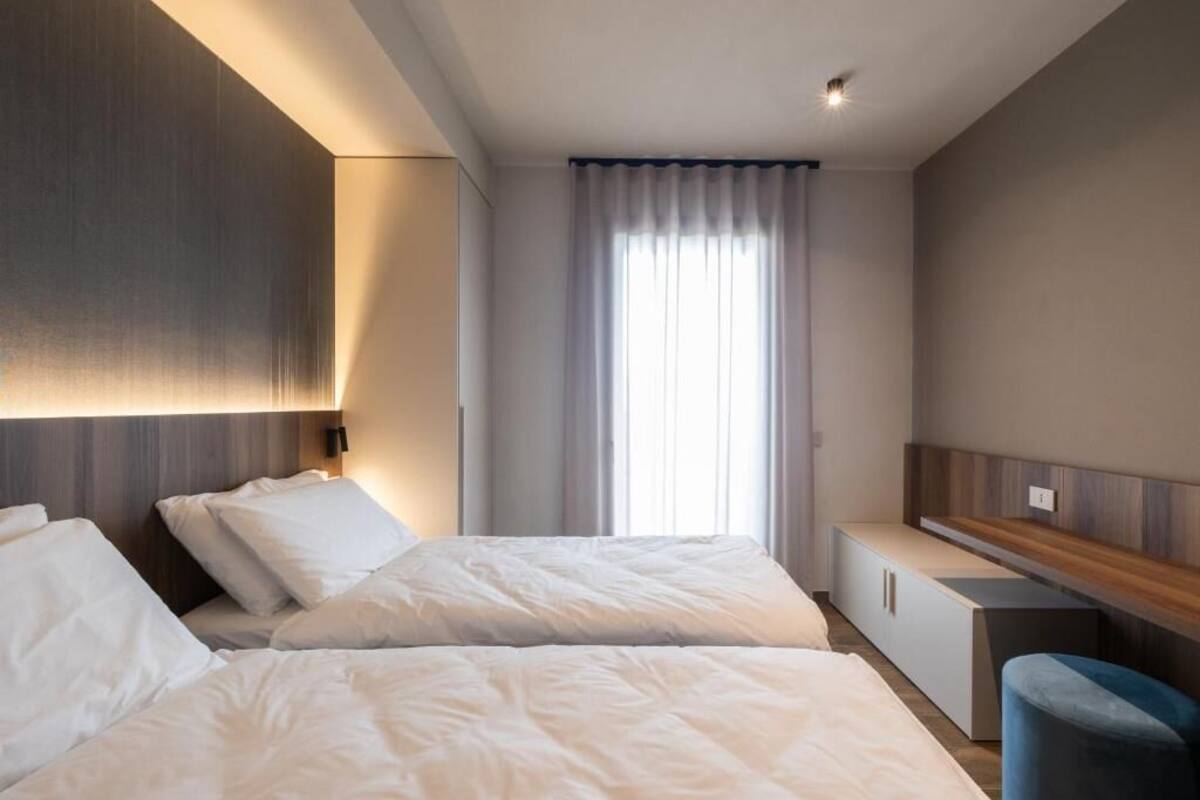 A modern hotel room with two beds, a desk, and a window with curtains.