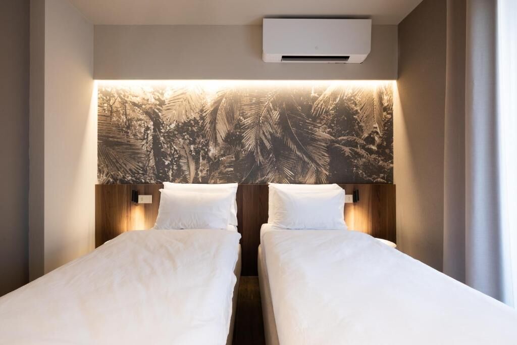 A hotel room with two single beds, a large wall mural, and an air conditioning unit.